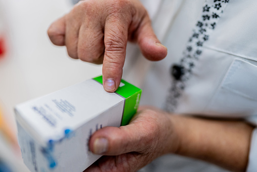 Imagem em close-up mostrando as mãos de uma pessoa segurando uma caixa de medicamento, com o dedo indicador apontando para os detalhes da embalagem onde as informações de registro Anvisa devem ser verificadas.