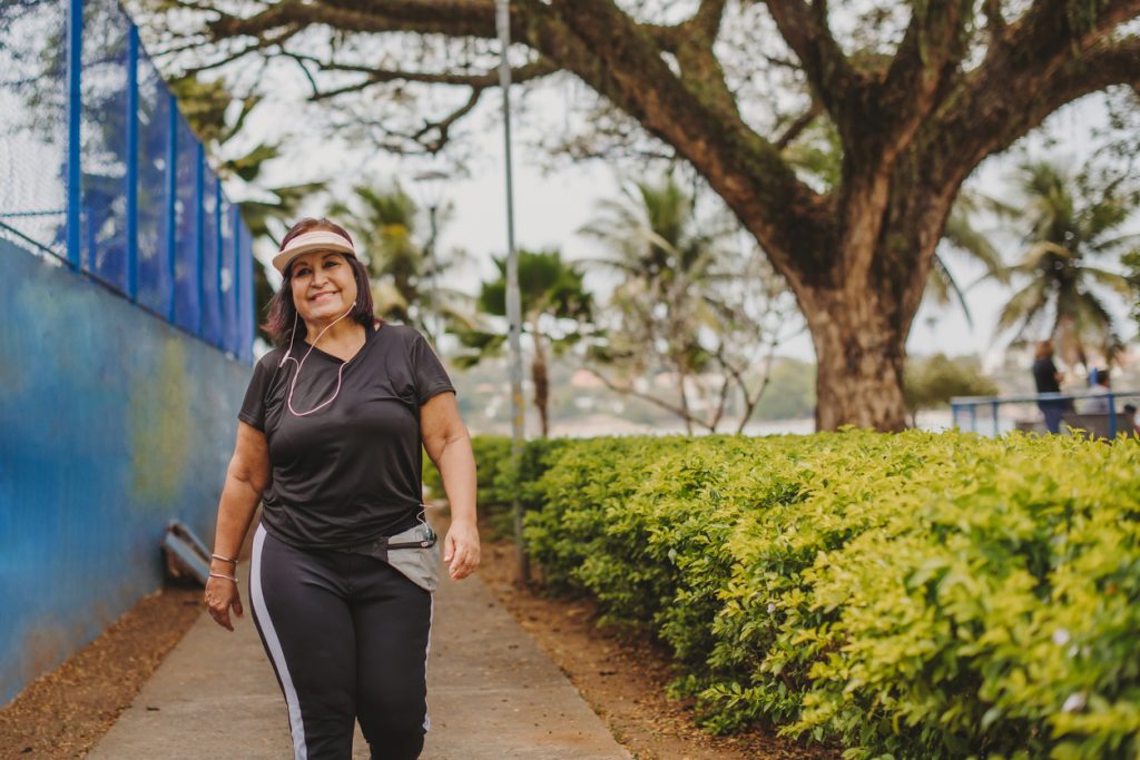 Mulher madura praticando caminhada ao ar livre em um parque, sorrindo e demonstrando qualidade de vida e saúde da mulher através do movimento.