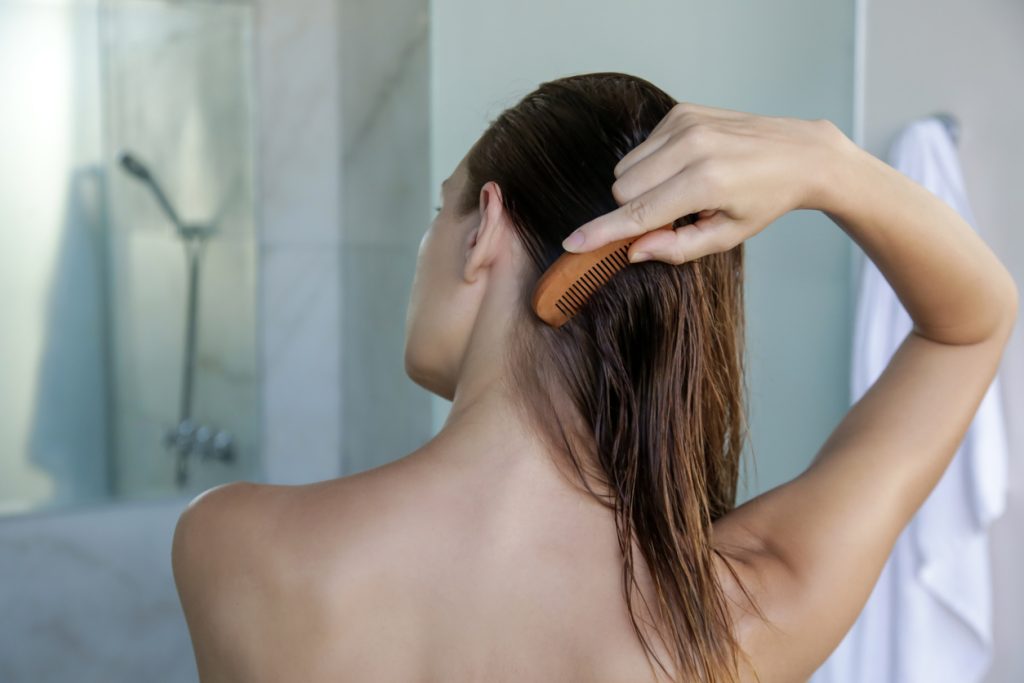 Mulher penteando cabelo no banho, indicando cuidados contra queda de cabelo