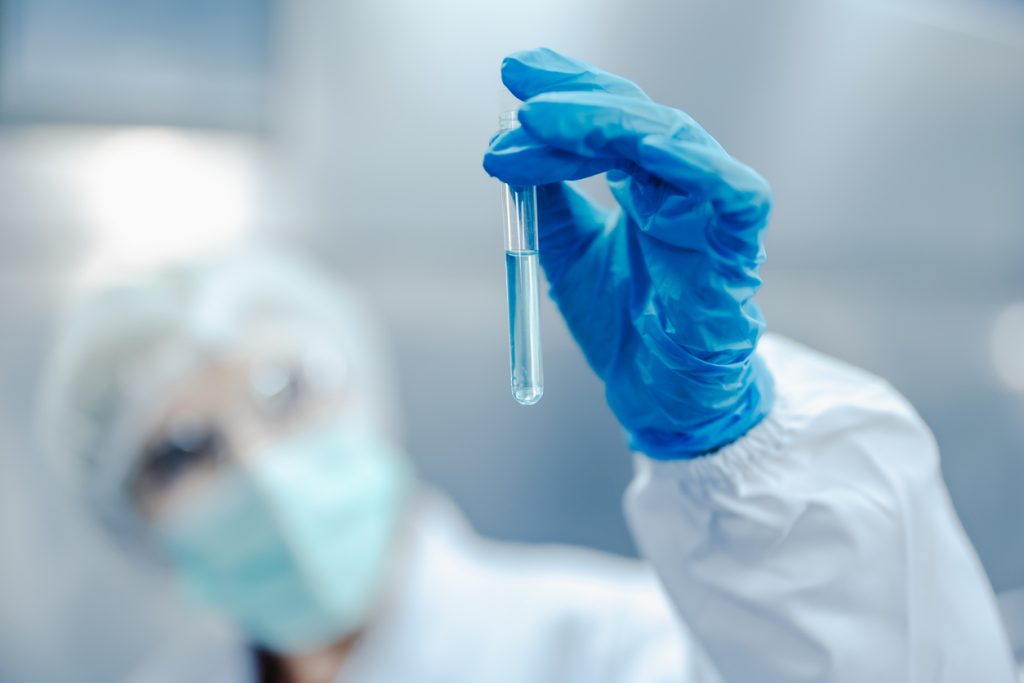 Profissional com luvas azuis segurando tubo de ensaio com líquido em laboratório