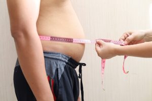Médico utiliza fita métrica para medir a circunferência abdominal de paciente, avaliando riscos de saúde.