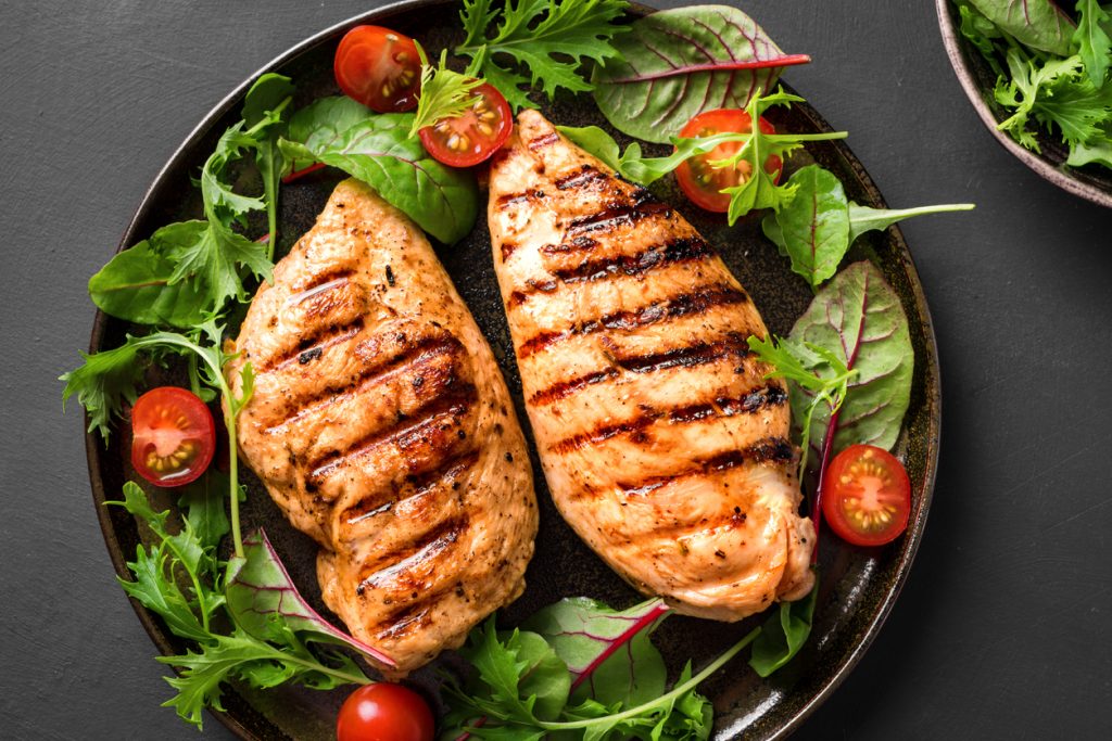 Prato com frango grelhado e salada como fonte de proteína diária.
