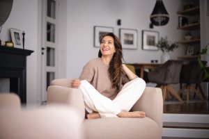 Mulher jovem sorridente sentada de forma confortável em uma poltrona em casa, representando bem-estar e equilíbrio na saúde da mulher.