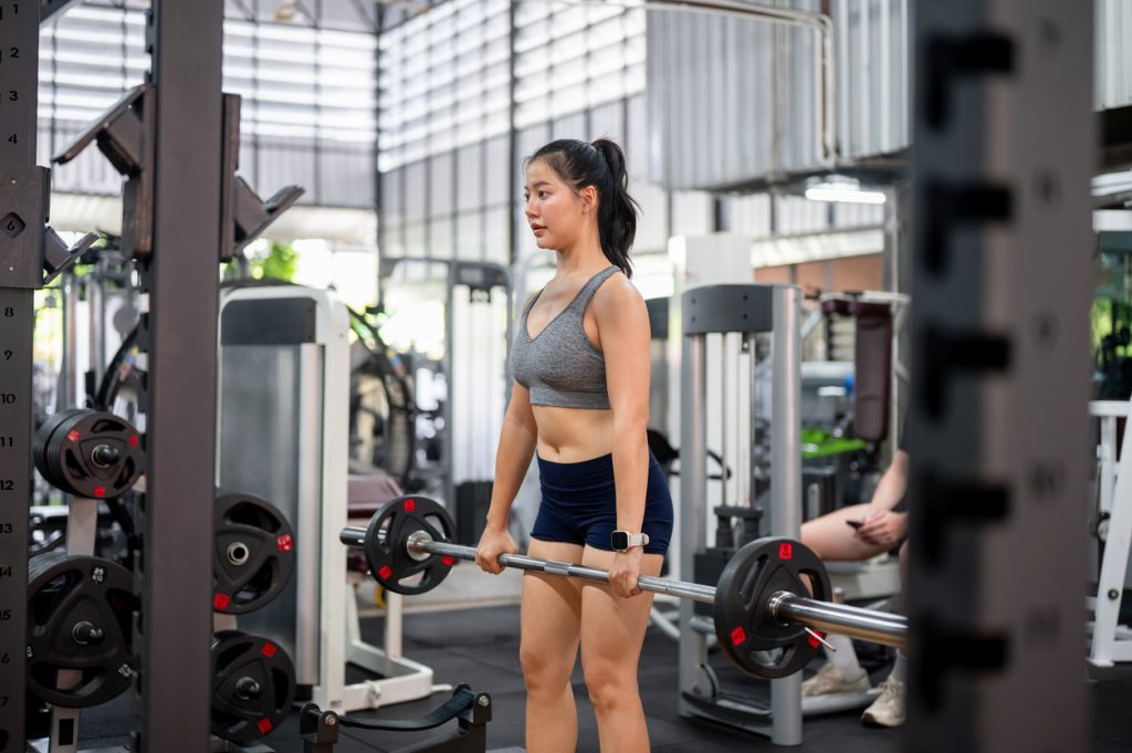 Mulher com descendência oriental treinando com barra na academia