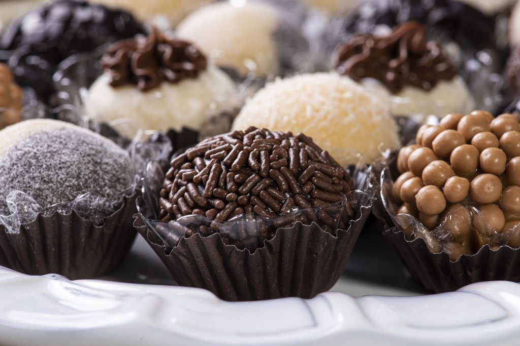 Imagem em close-up de vários doces de festa, como brigadeiros tradicionais e beijinhos em forminhas, cobertos com granulado e bolinhas de chocolate. Eles representam alimentos ricos em açúcar que devem ser evitados na dieta para diabetes para não prejudicar o controle glicêmico.