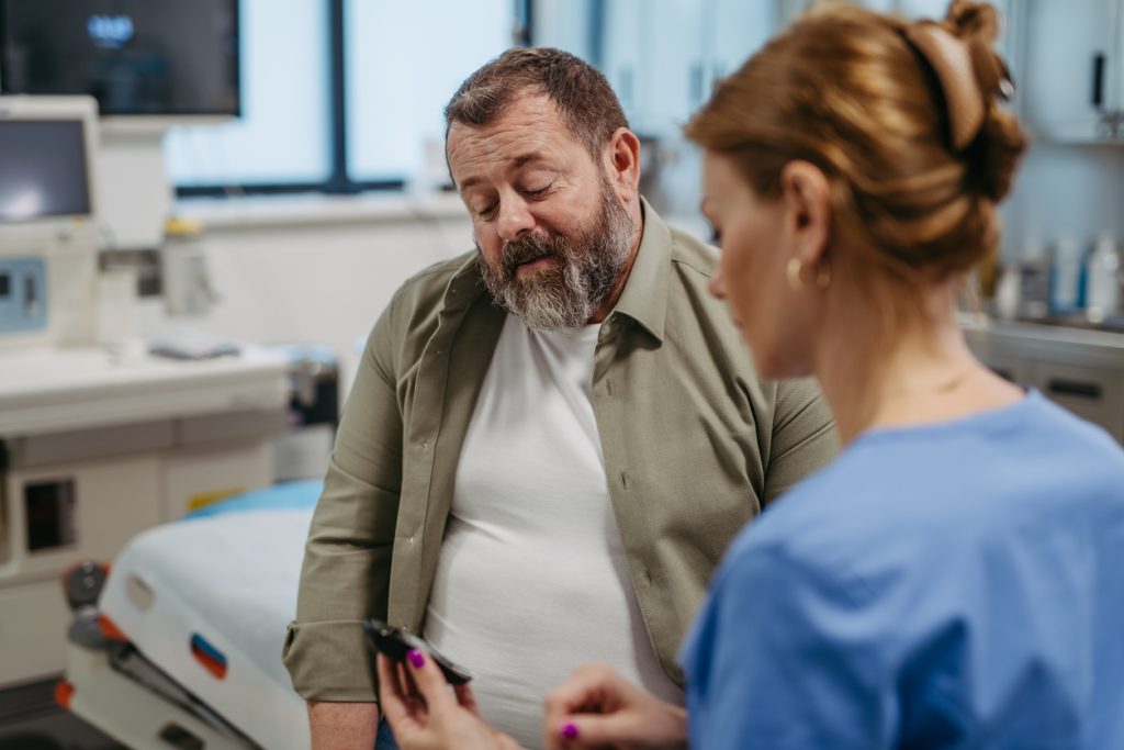 Homem com sobrepeso em consulta médica conversando com uma profissional de saúde sobre o controle da glicemia e resistência à insulina.