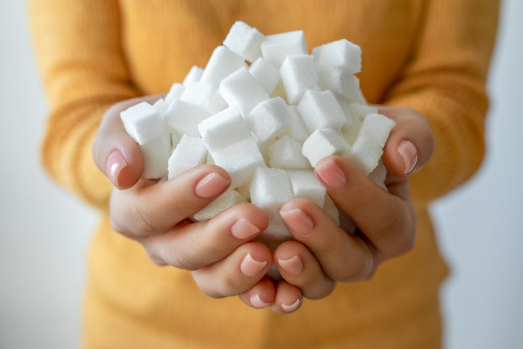 Close em mãos segurando uma grande quantidade de cubos de açúcar branco, ilustrando o alto consumo de açúcar que atua como um fator de risco para o pré-diabetes.