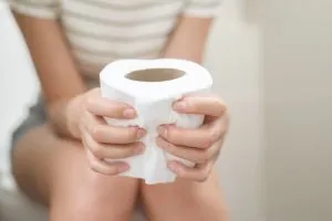 Mulher segurando um rolo de papel higiênico com as duas mãos, representando as dificuldades e o desconforto causados pela constipação.