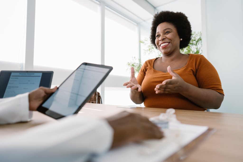 Mulher sorridente conversando com profissional de saúde que segura um tablet durante consulta, ilustrando a escolha entre liraglutida ou semaglutida