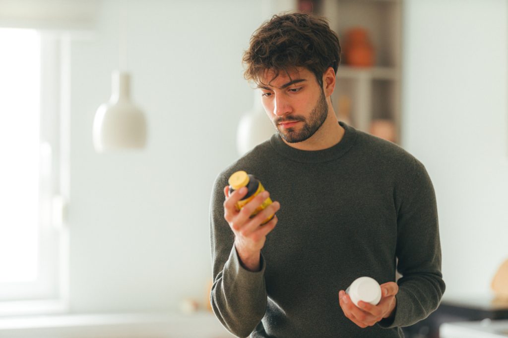 Homem observando com atenção o rótulo de um frasco de suplemento em casa, ilustrando a busca pelos benefícios do ômega 3