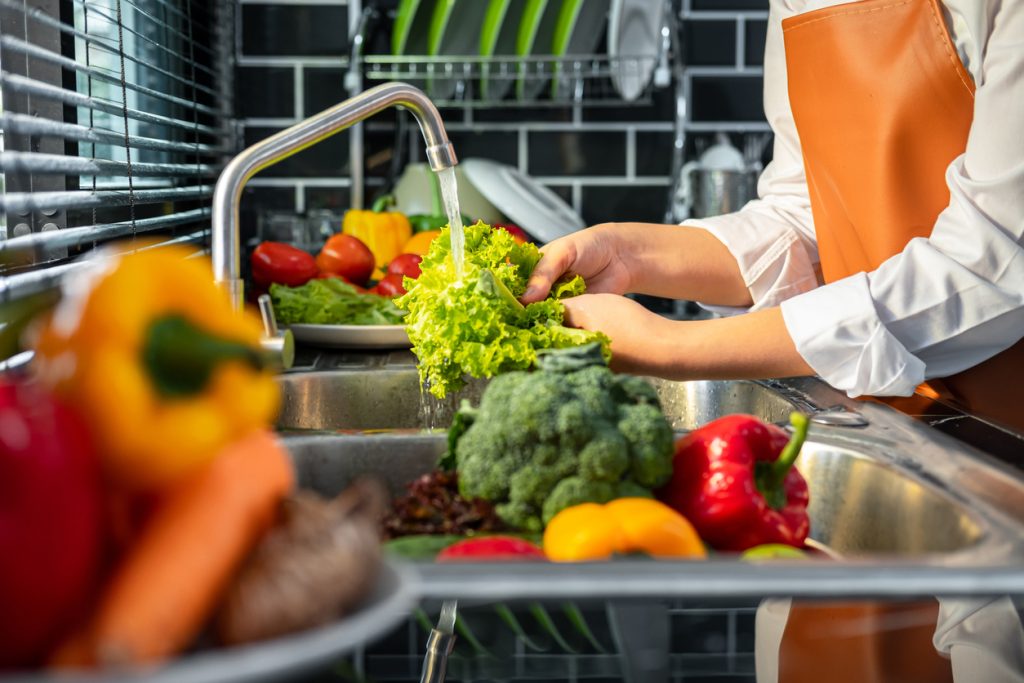 Pessoa lavando folhas e legumes frescos na pia da cozinha, ilustrando a importância da alimentação saudável no controle do diabetes