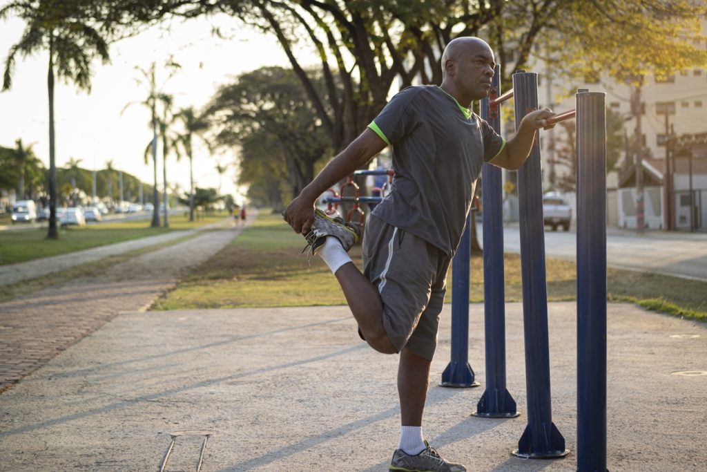 Homem se alongando ao ar livre antes de treinar em um parque ao entardecer, ilustrando a importância da atividade física no controle do diabetes