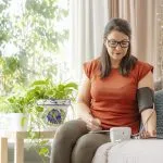 Mulher medindo a pressão arterial em casa e anotando os valores, ilustrando o controle da hipertensão associado ao emagrecimento